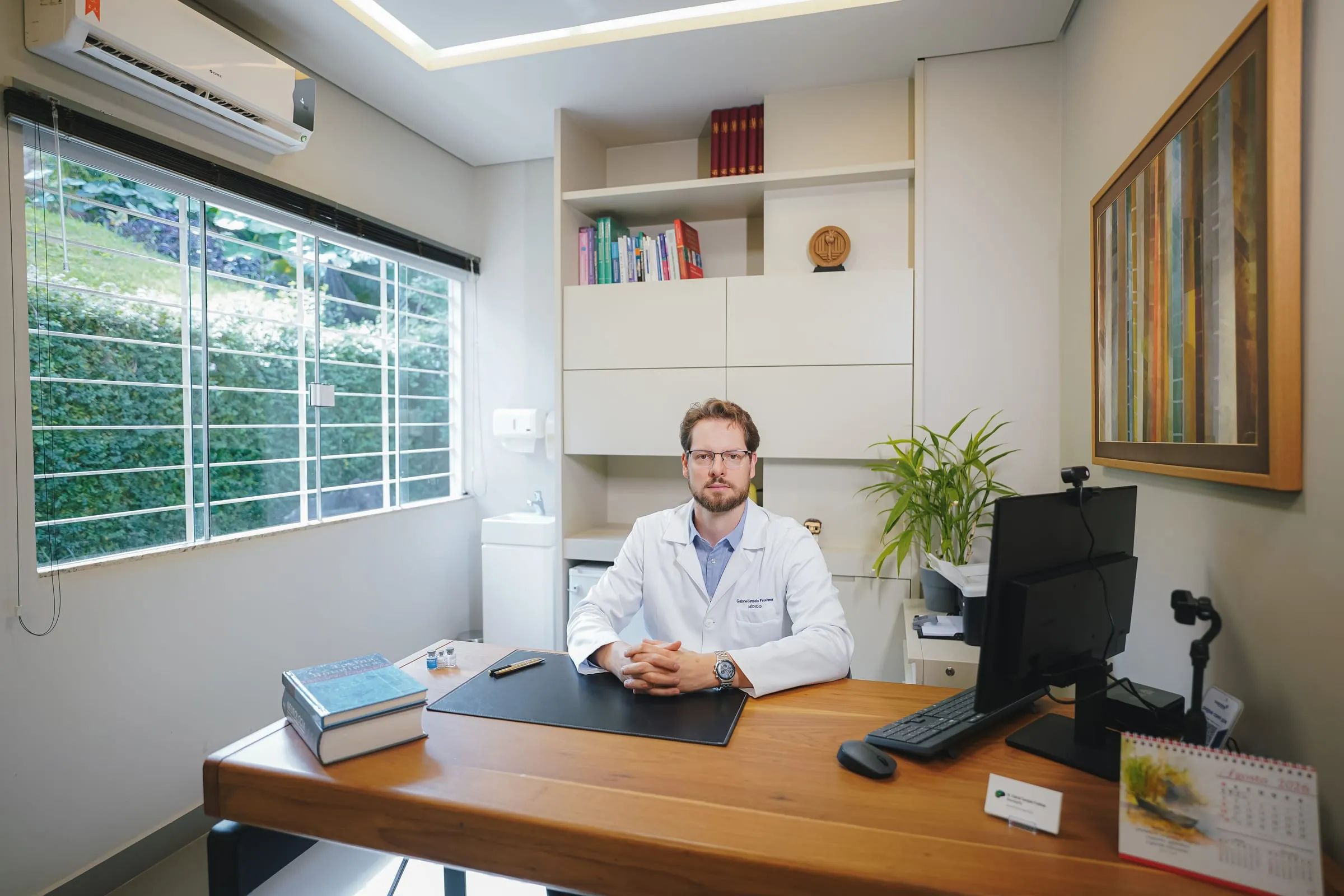 Consultório com mesa de madeira, estante de livros e janela para o jardim