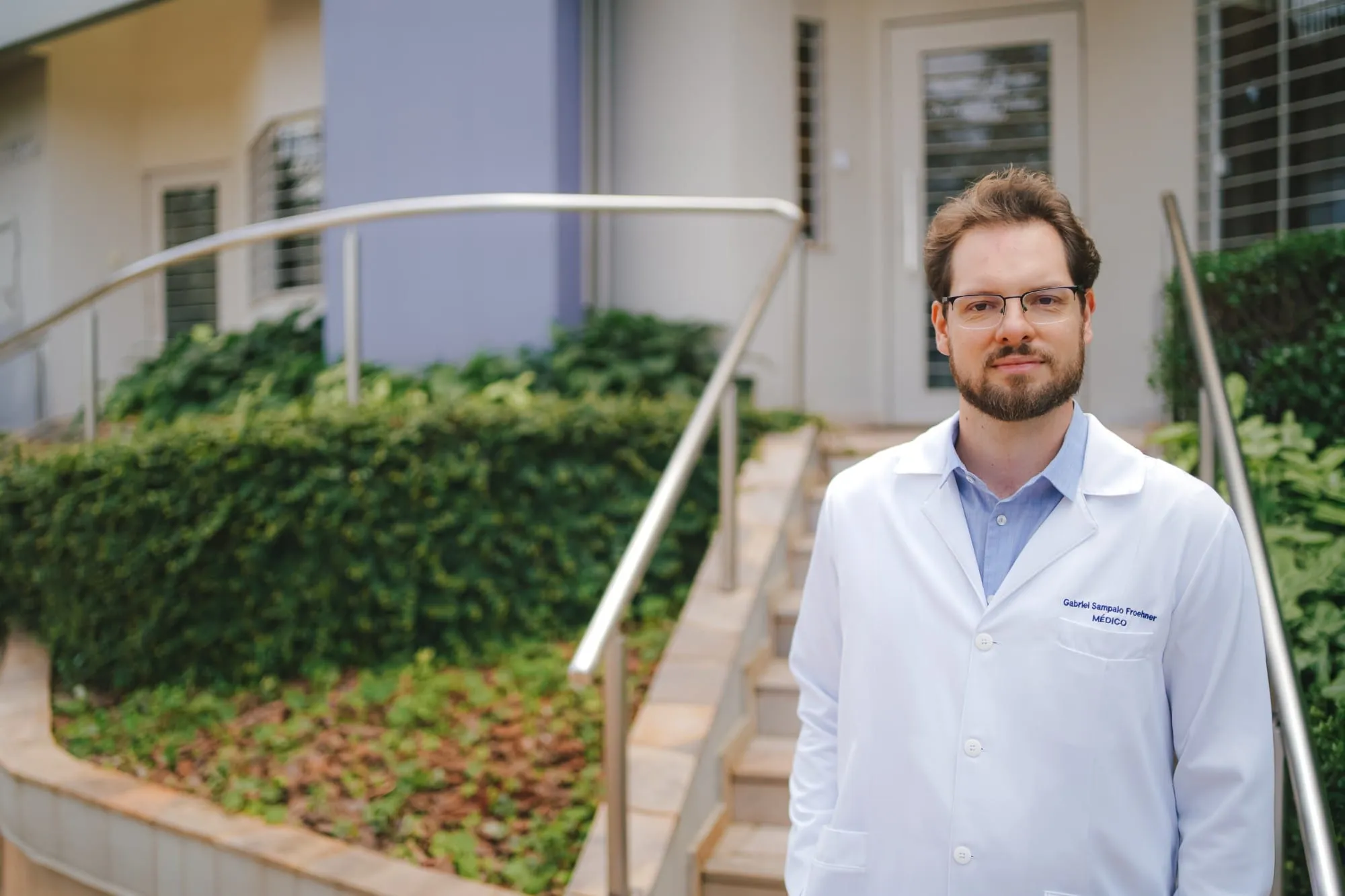 Dr. Gabriel Sampaio Froehner na entrada da clínica, de jaleco