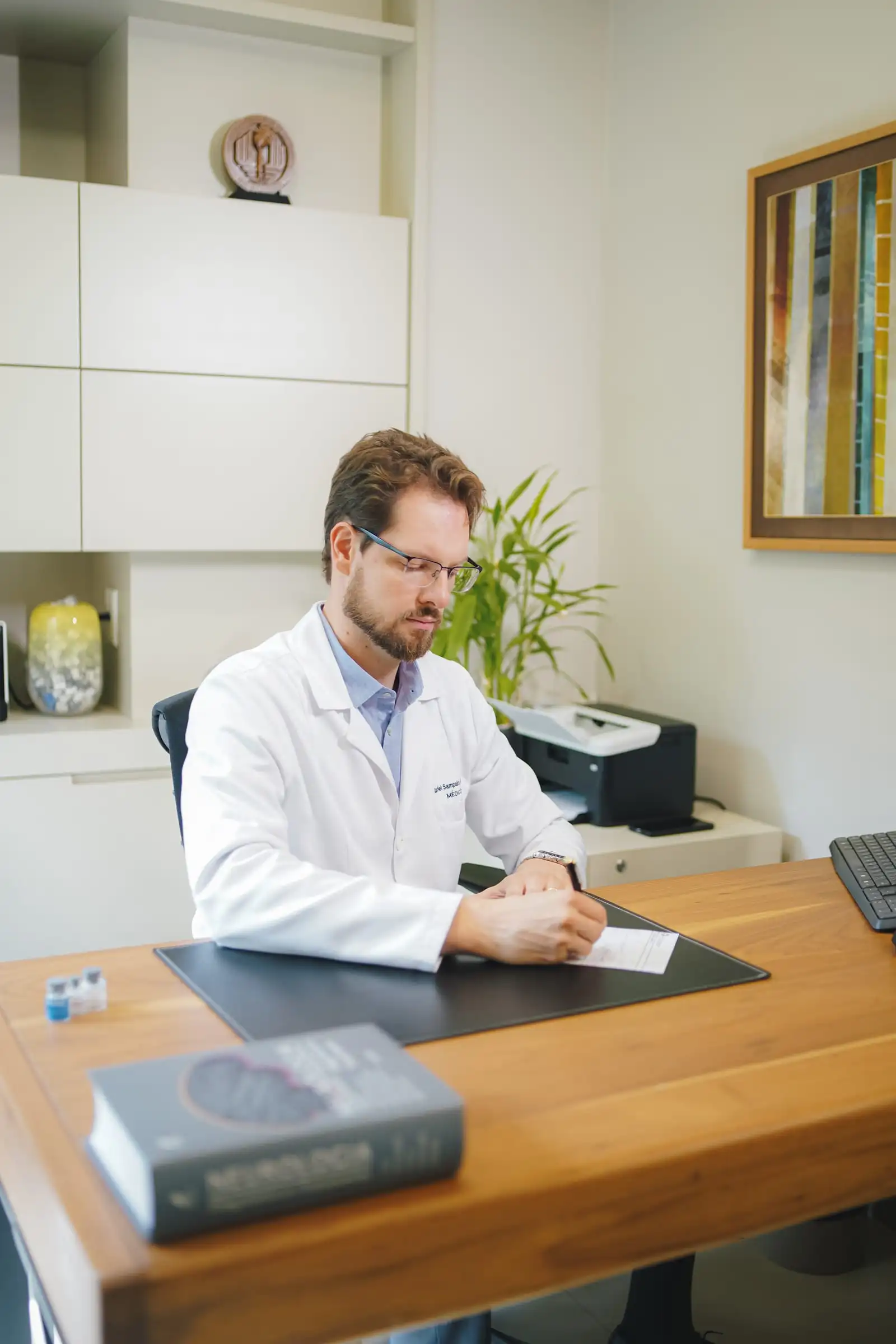 Dr. Gabriel Sampaio Froehner escrevendo uma prescrição no consultório