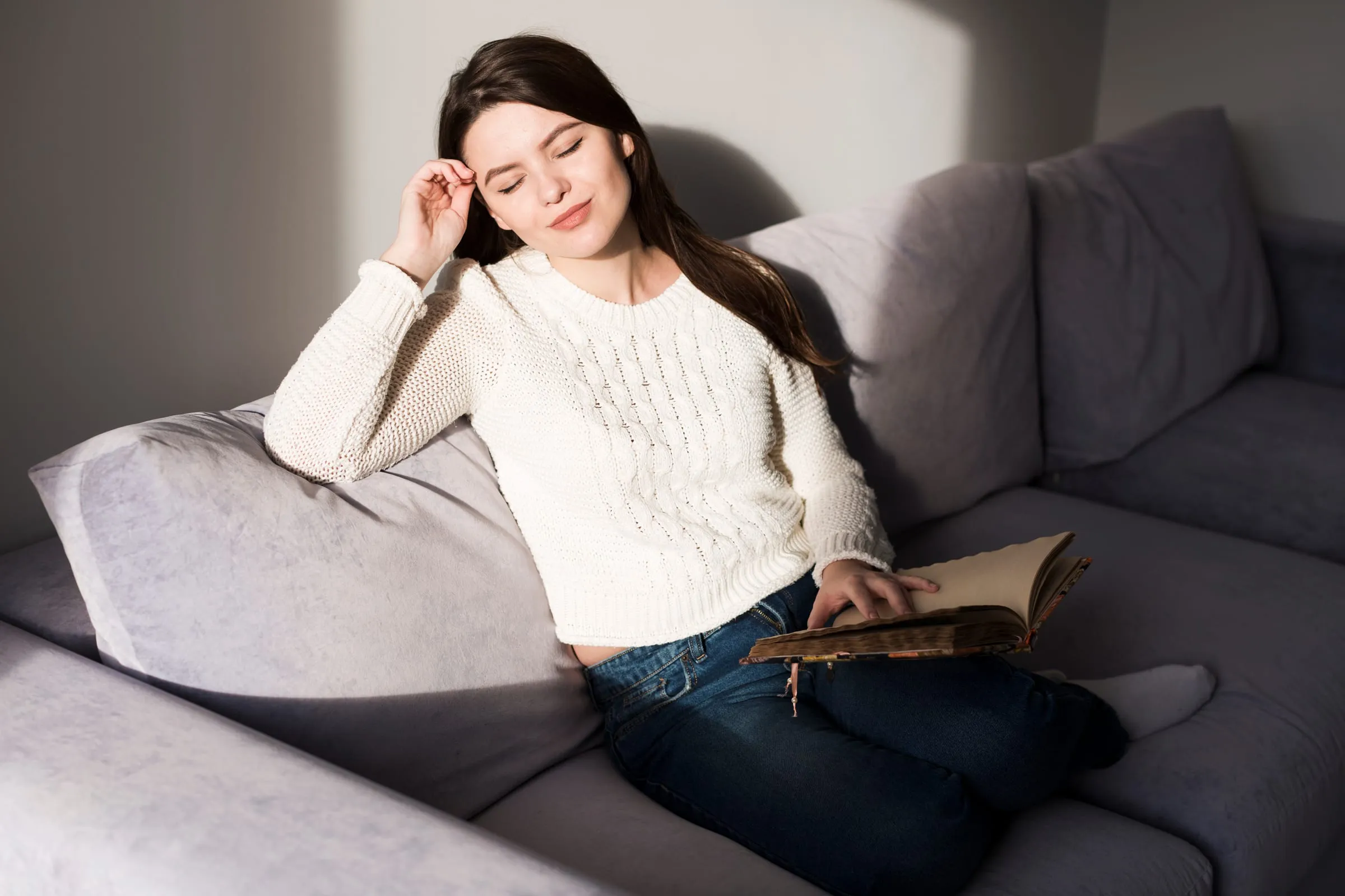 Mulher jovem descansando no sofá de casa com um livro