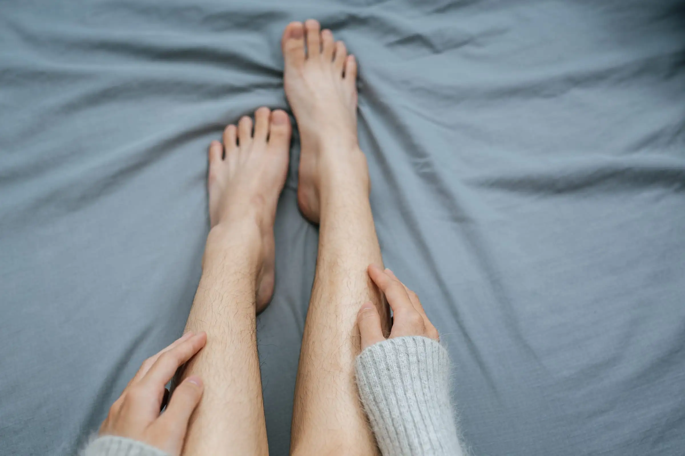 Mãos tocando a perna, com os pés apoiados sobre a cama