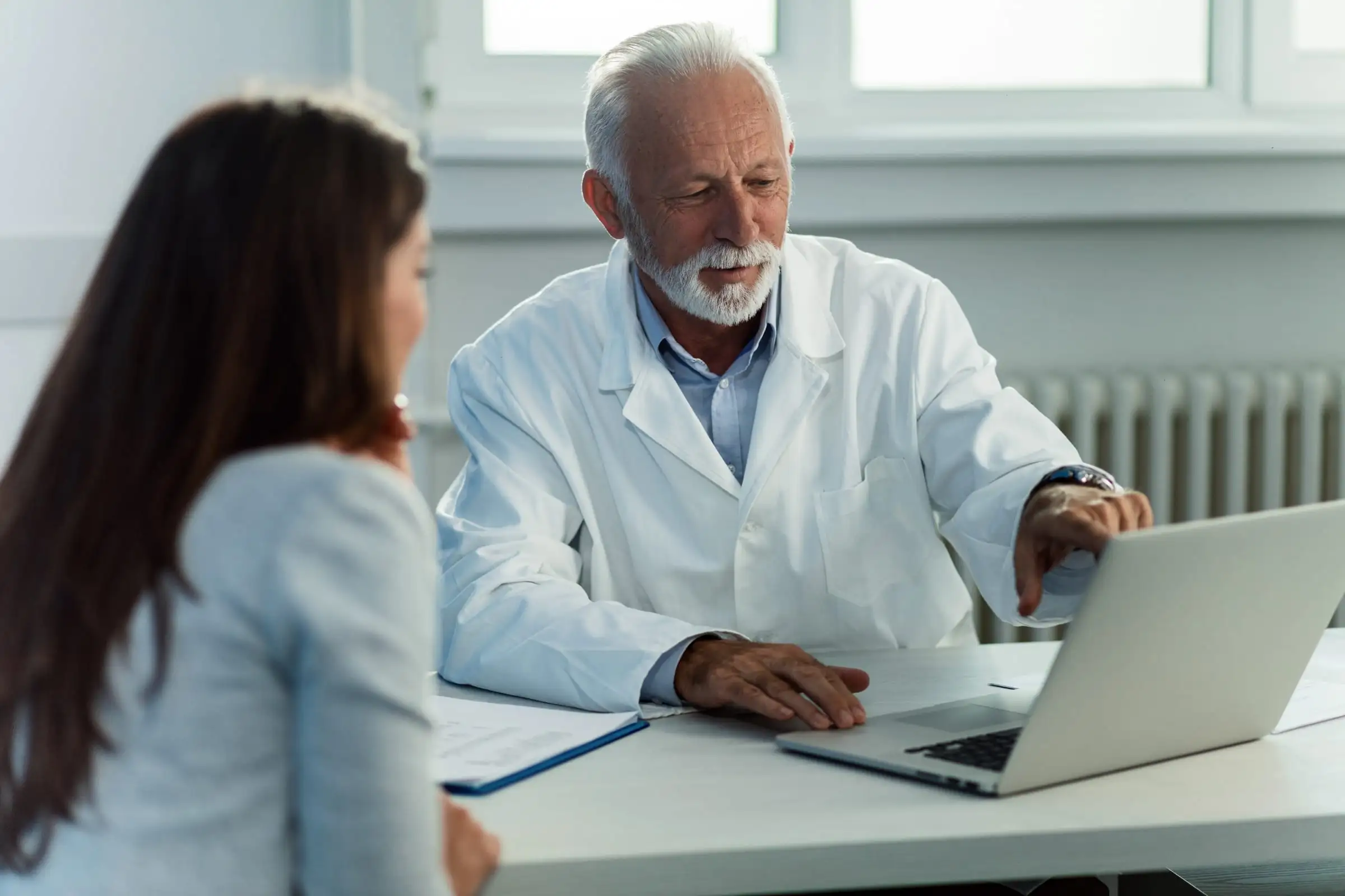 Médico conversando com uma pessoa diante do computador no consultório