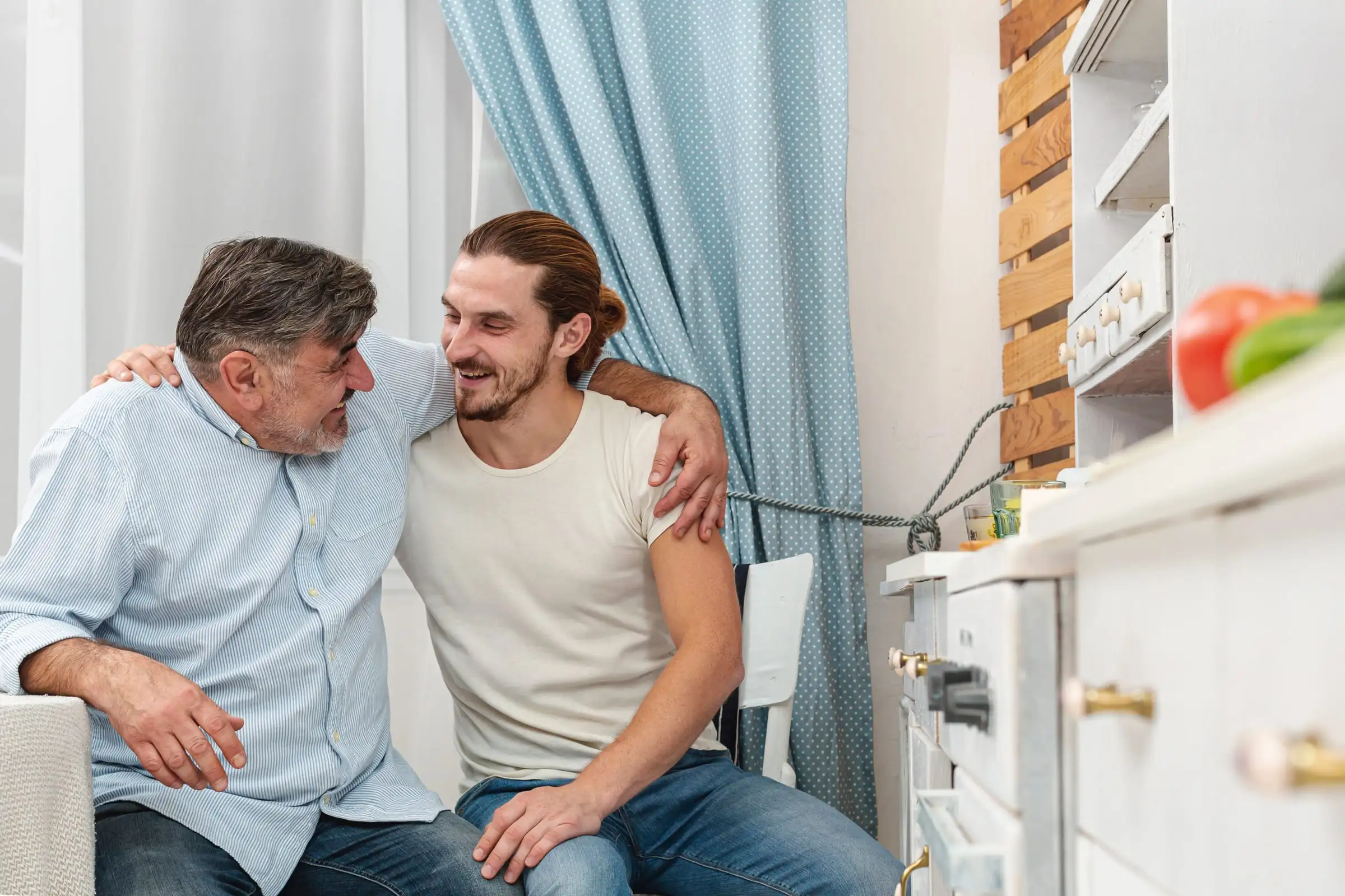 Pai e filho adulto abraçados e sorrindo na cozinha de casa