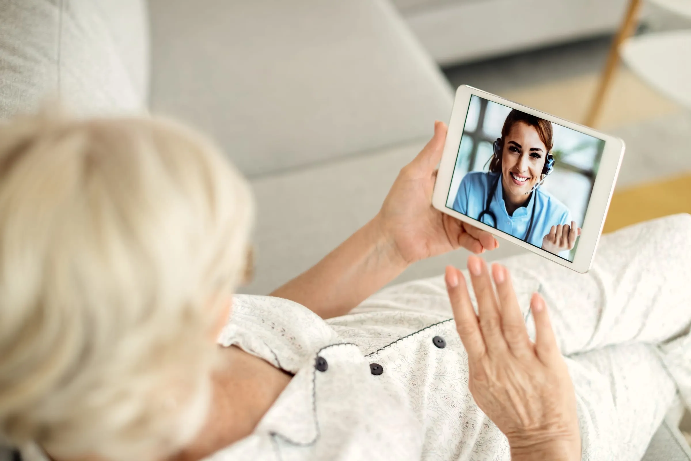 Senhora no sofá de casa em videochamada pelo tablet